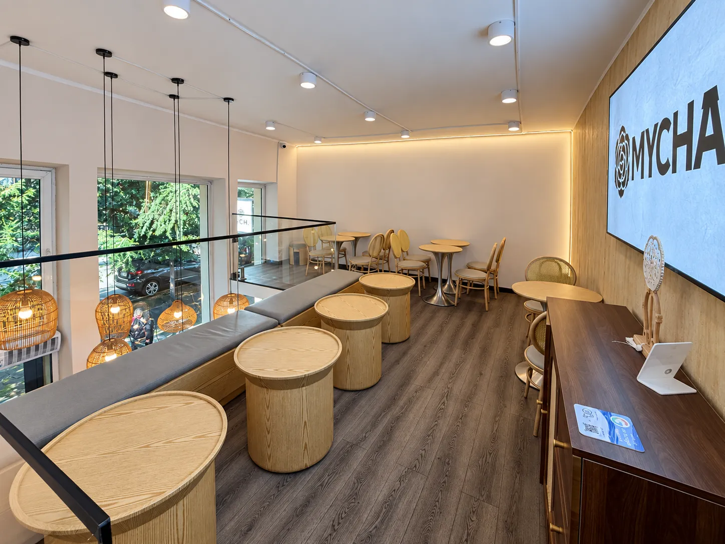 Upper-floor MYCHA seating with round wooden tables and a glass railing