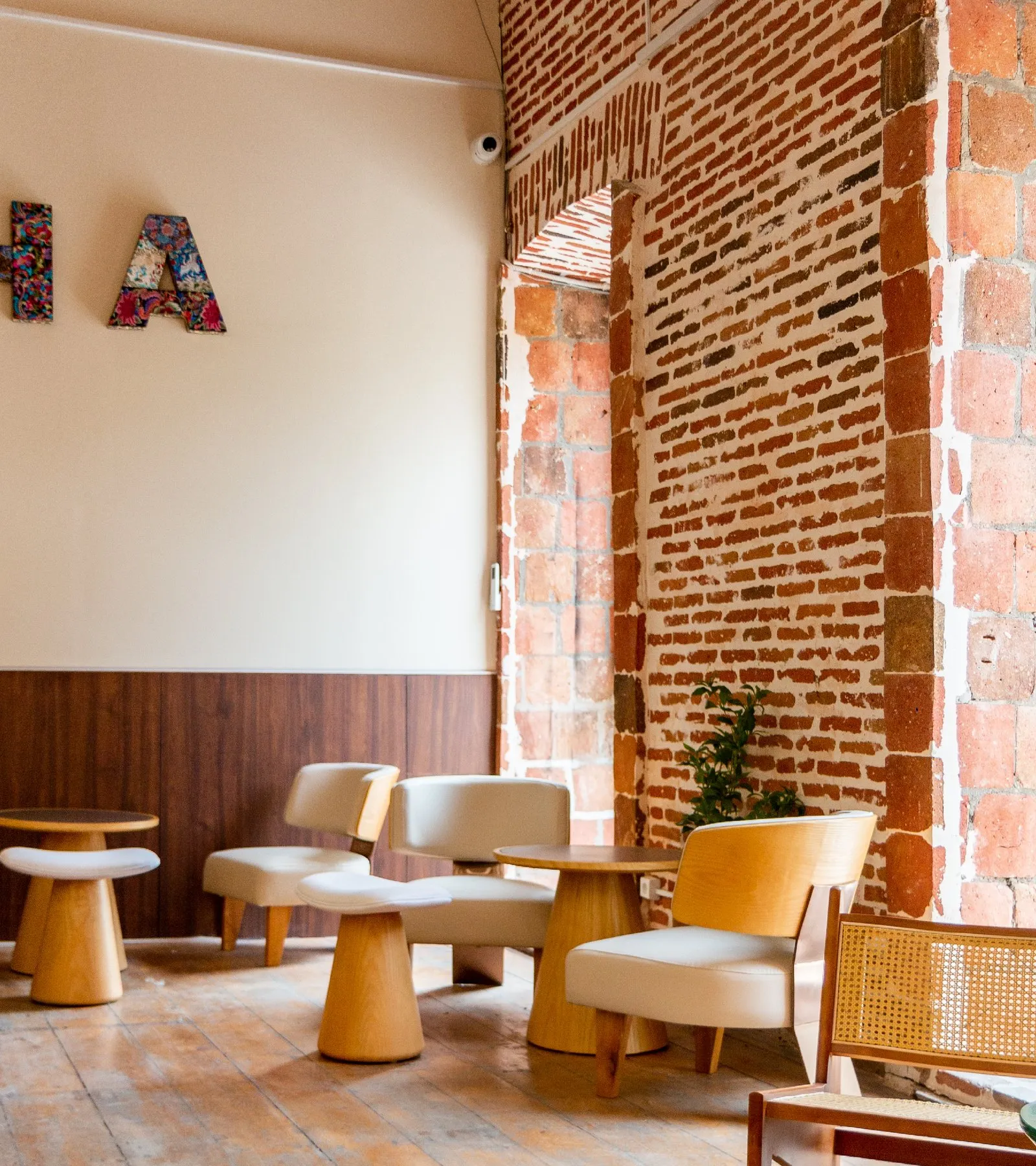 Timber armchairs and round tables beside an exposed brick wall