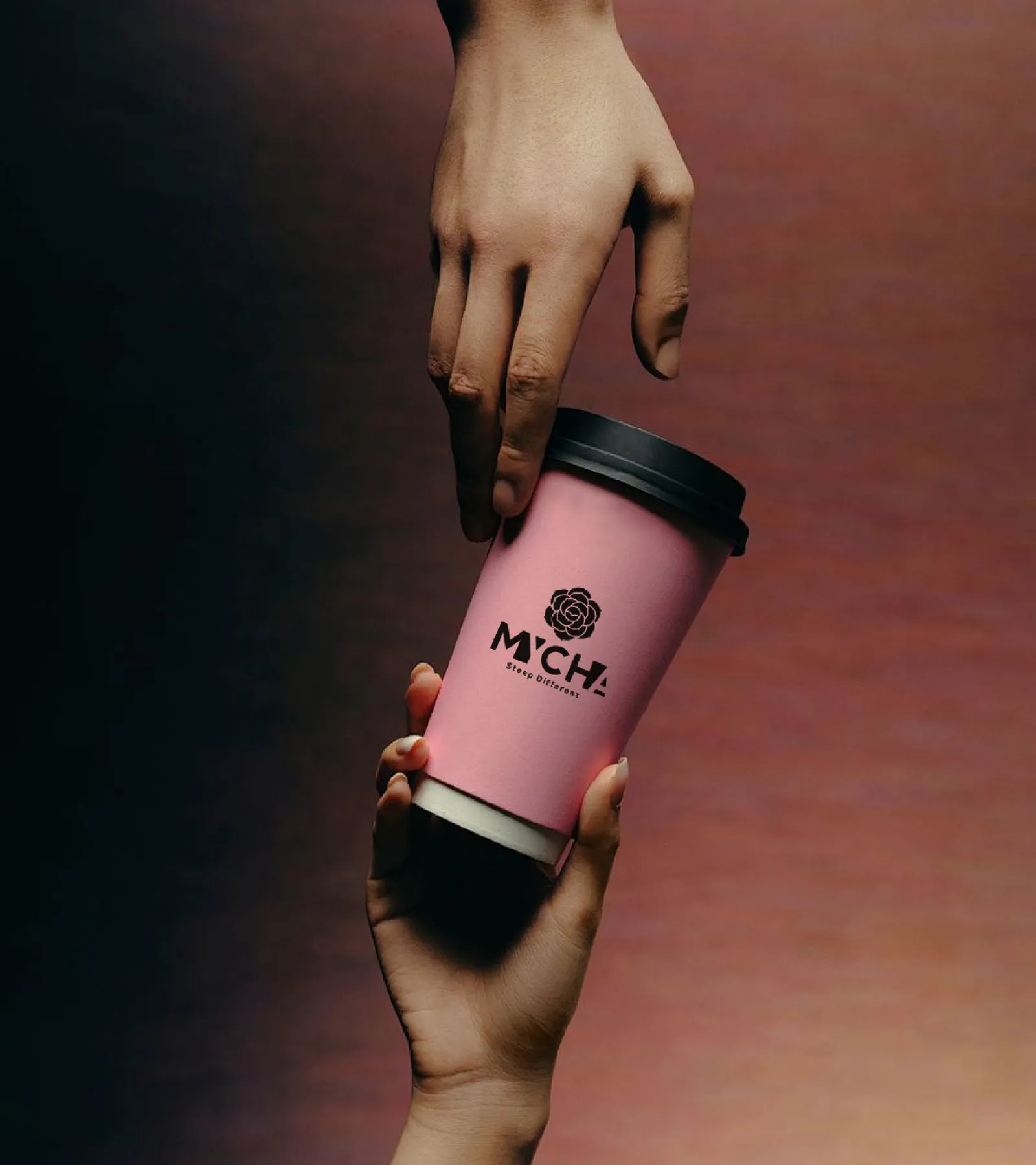 One hand passing a pink MYCHA cup to another against a dark ground