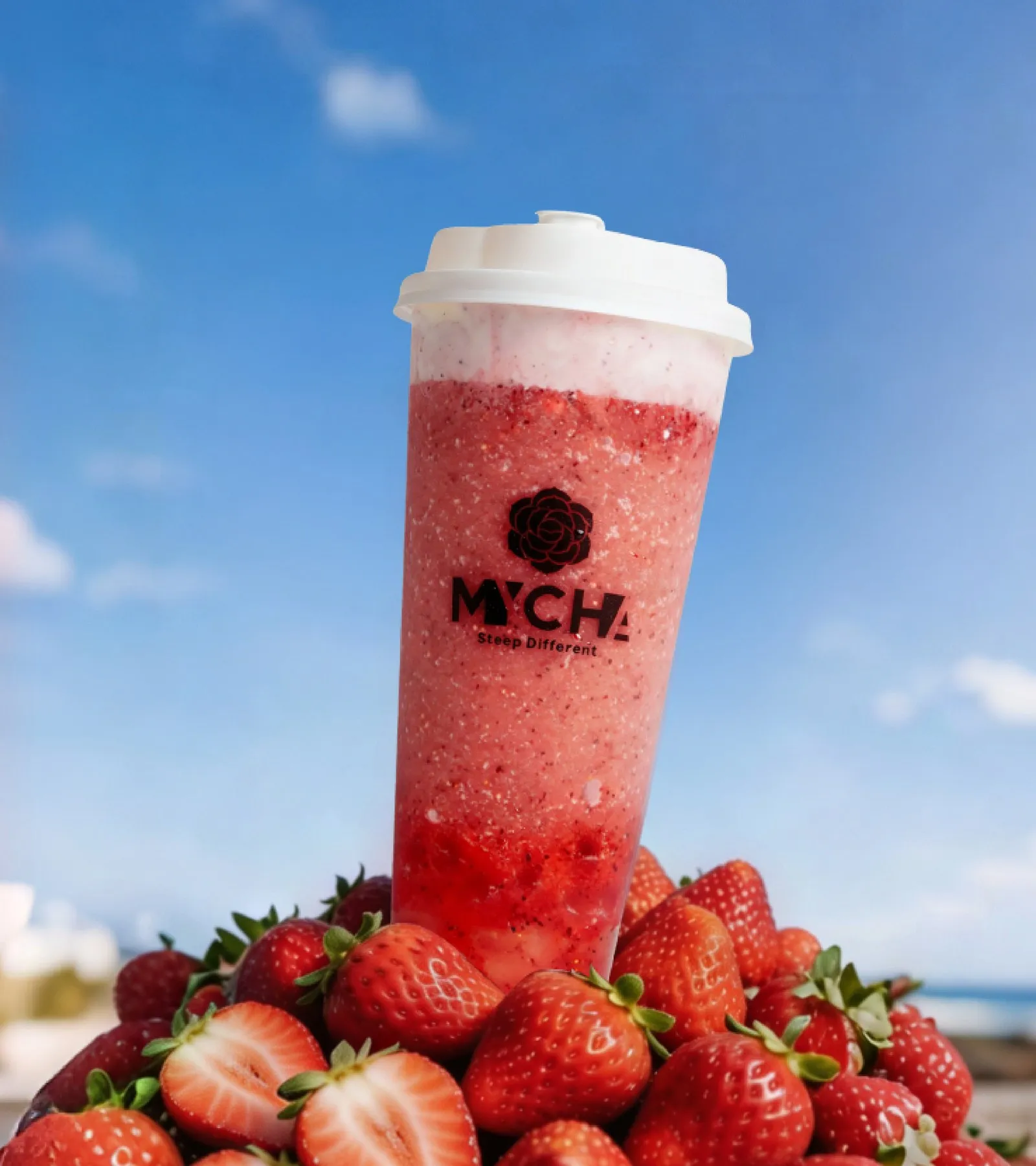 A MYCHA strawberry frappuccino standing on a pile of fresh strawberries by the sea